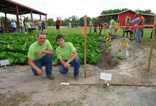 High school agriculture students kneeling in front of the crops with a new irrigation system.