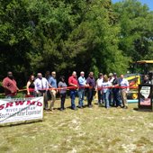 Individuals posing in front of a red ribbon with a sign saying "thank you" to the Suwannee River Water Management District. 