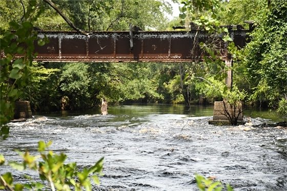 Rapids flowing under an old bridge with bright trees along the riverbank.