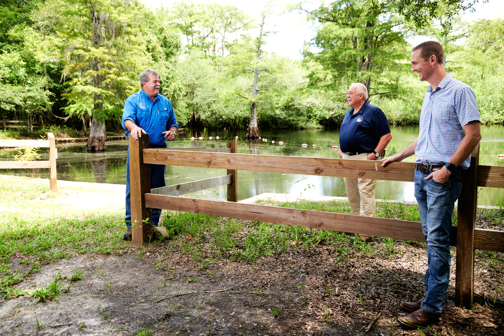 Three men standing around a fence with a spring in the background